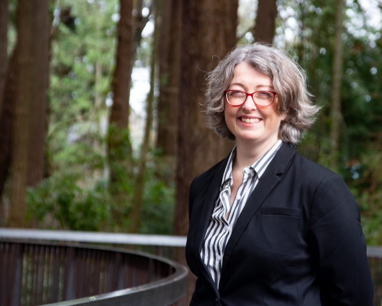 Image of Steph wearing a black blazer and smiling in front of a number of larger trees